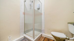 Kylpyhuone, jossa on lasiseinällä varustettu suihku, wc ja tervetulomatto.