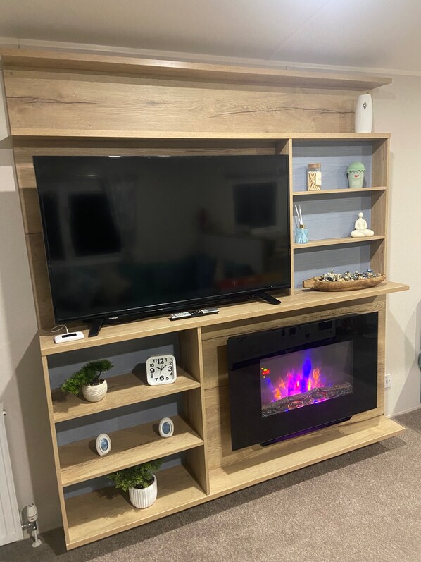 Un mueble de madera para entretenimiento con un televisor de pantalla plana, una chimenea y estantes con objetos decorativos.