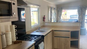 A compact kitchen with a microwave, stove, sink, and wooden cabinets.
