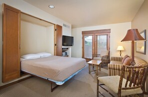 Una habitación de hotel con cama, televisión, escritorio, silla y lámpara.