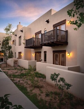 Un edificio de varios pisos con balcones, un patio con plantas e iluminación exterior.
