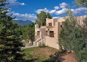 A modern building with a flat roof, multiple windows, and a surrounding landscape with trees and mountains.