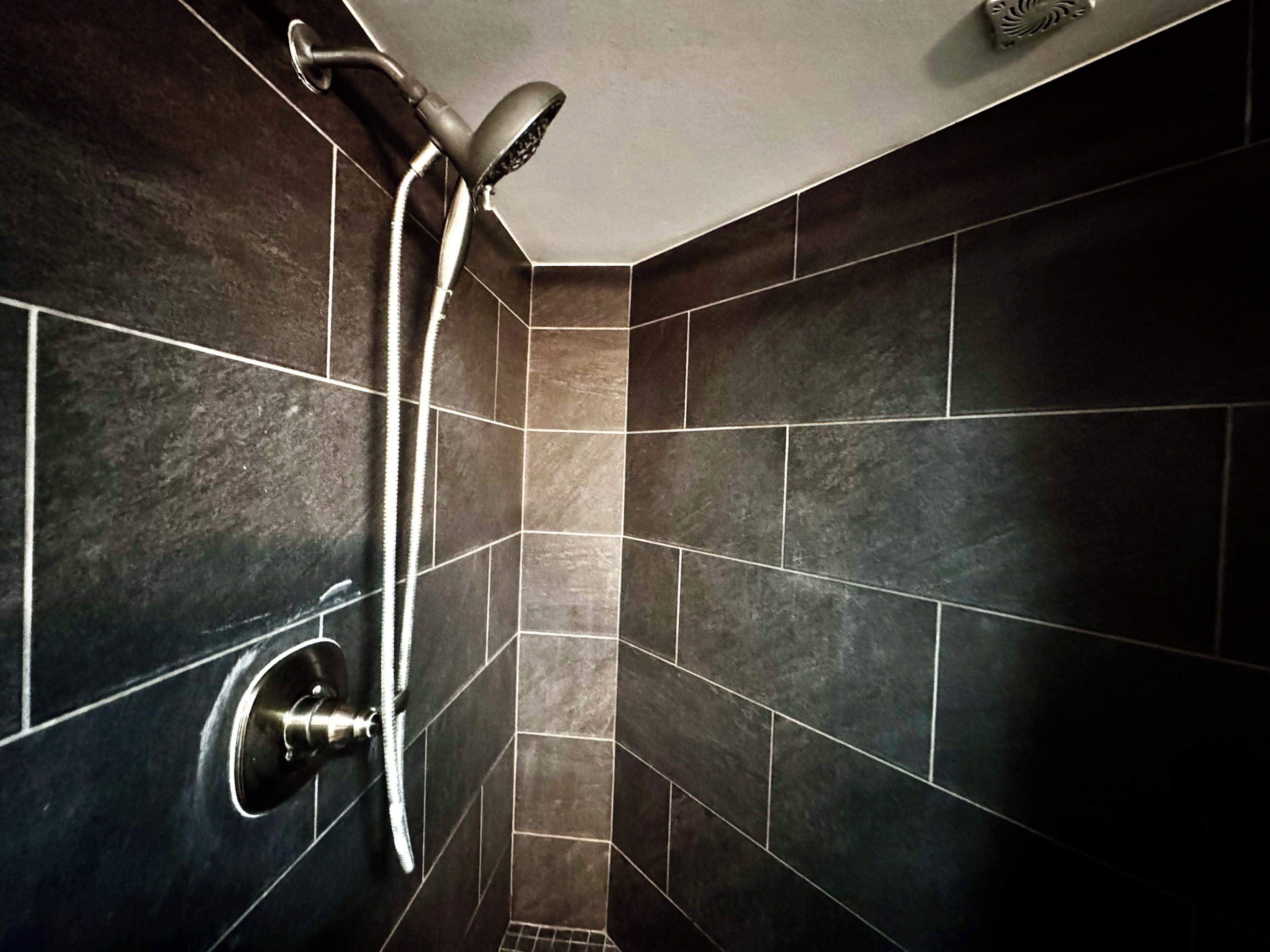 A shower with a handheld showerhead and a wall-mounted faucet in a tiled bathroom.