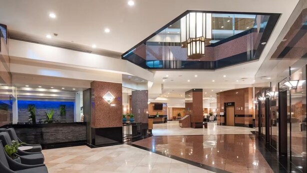 A modern hotel lobby with a reception desk, seating area, and a glass staircase. - Penthouse Loft LargeTerrace2-bedroom Kitchen Seaside  HPU&Cruise  8 person (Honolulu)