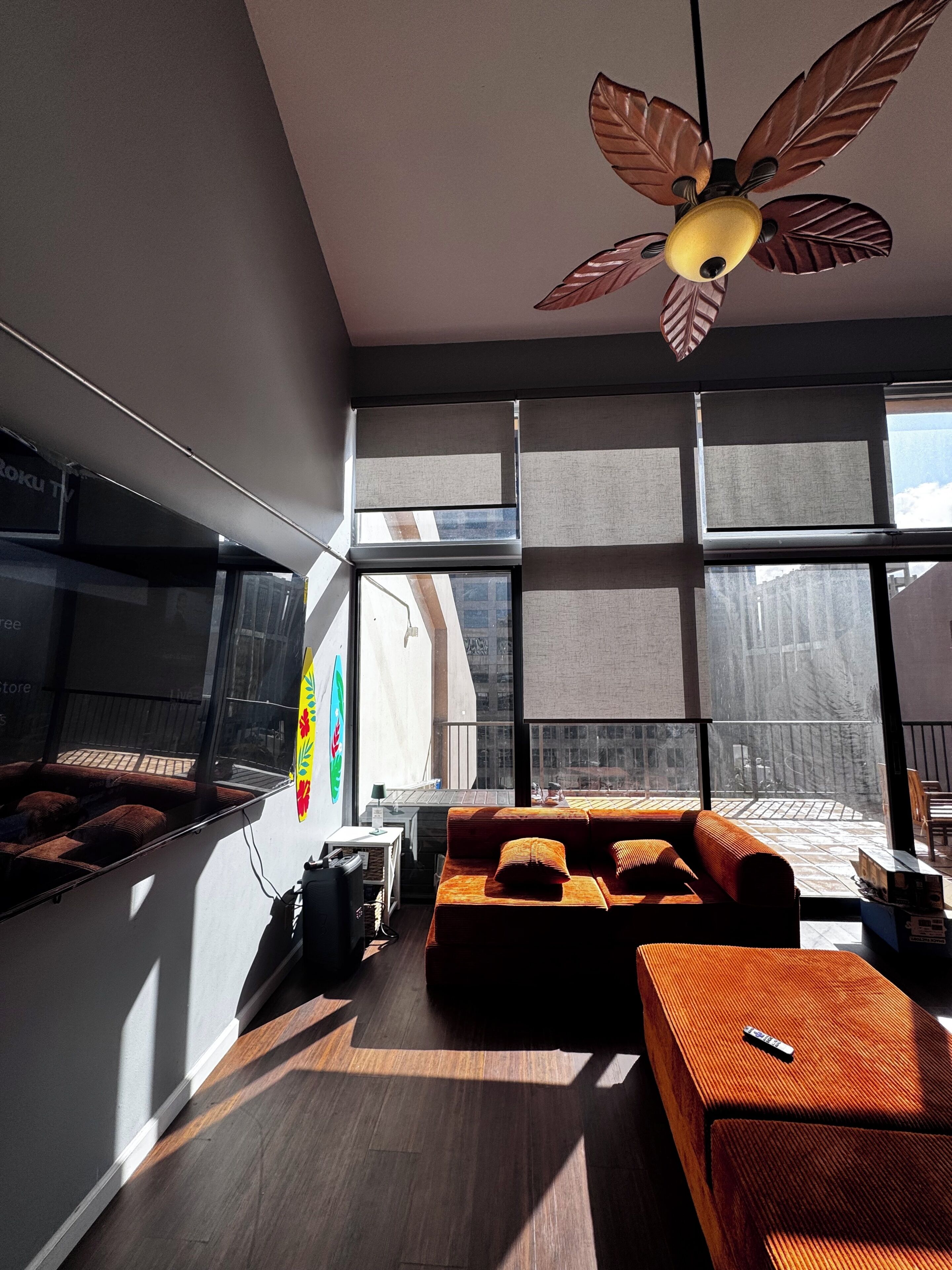A modern living room with a sofa, a coffee table, a ceiling fan, and large windows.