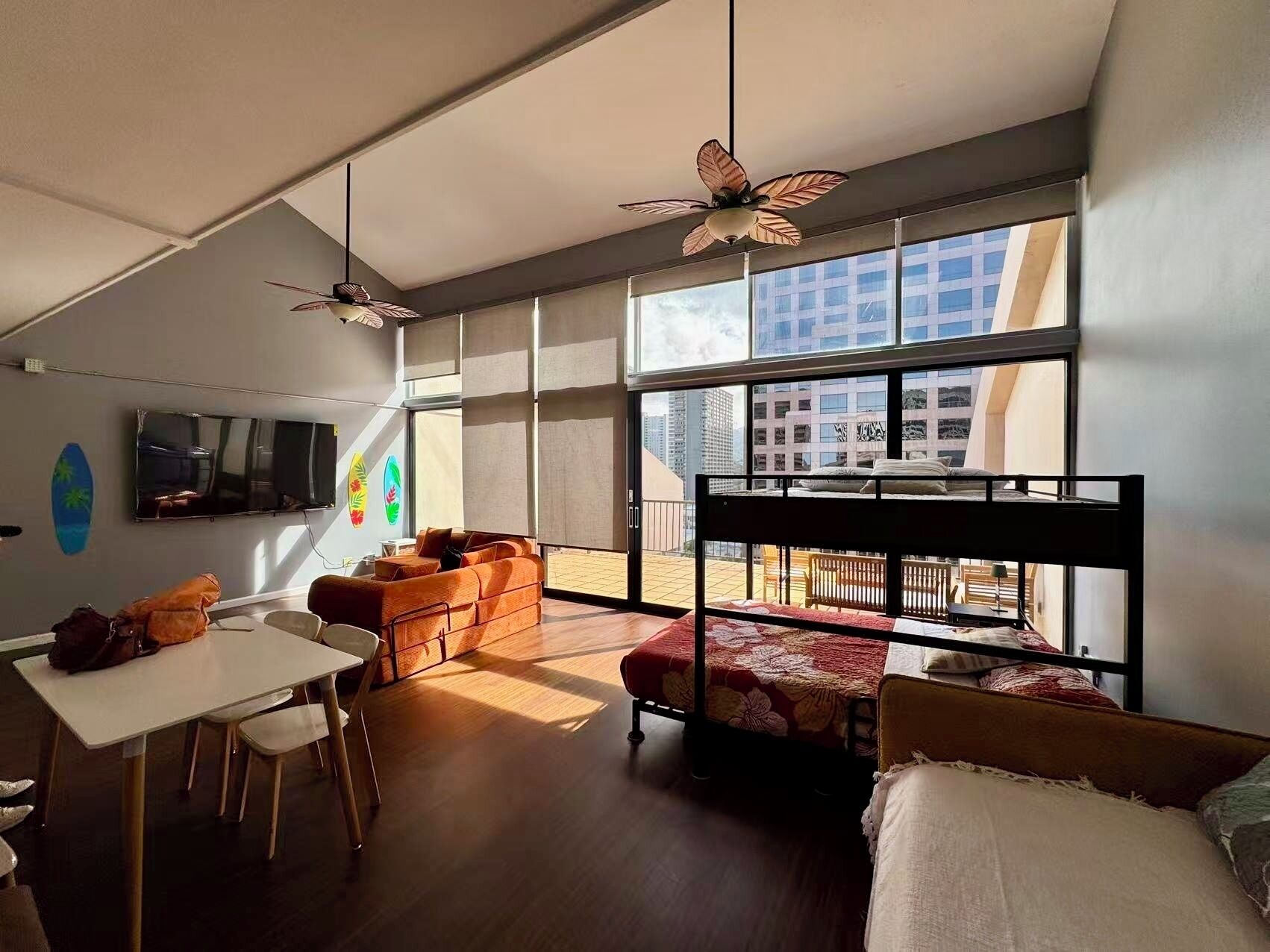 A modern room with a bunk bed, a dining table, and chairs. There is a TV mounted on the wall and a ceiling fan.