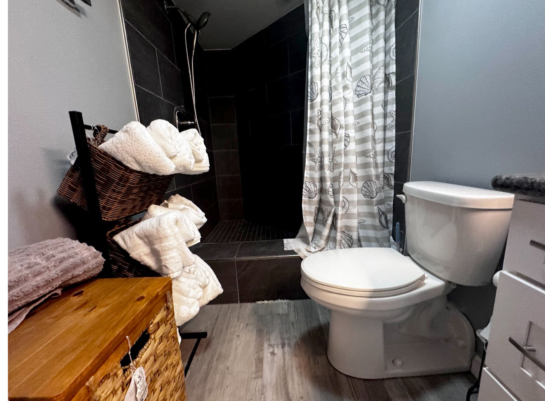 Ein Badezimmer mit Toilette, Duschbereich, einem Korbwäscheschrank mit Handtüchern und einem gestreiften Duschvorhang.