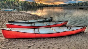 A calm lake with three red canoes on the shore, surrounded by dense forest and a dramatic sky. - Vancouver | Urban Group Retreat | Walkable + Sauna | 2BR (Vancouver)