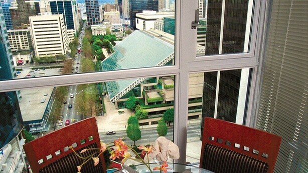 A dining table with chairs, a vase with flowers, and a city view through a large window. - Vancouver | Urban Group Retreat | Walkable + Sauna | 2BR (Vancouver)