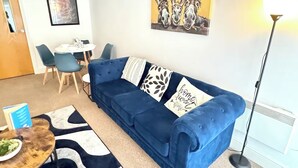 A living room with a blue sofa, a round coffee table, a painting of donkeys, and a floor lamp.