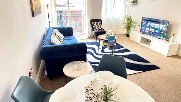 A living room with a sofa, chairs, a coffee table, a TV, and a view of buildings outside.