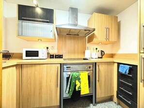 A compact kitchen with a microwave, toaster, kettle, and oven.