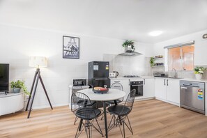 Et moderne køkken med hvide skabe, et sort køleskab, et spisebord med stole og en gulvlampe.
