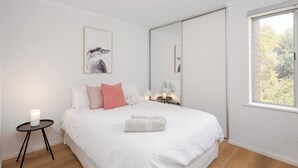 Un dormitorio con cama, mesita de noche con lámpara, espejo y ventana con vistas.