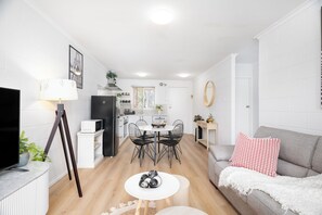 En moderne stue med et fladskærms-tv, et spiseområde med bord og stole, og en grå sofa med en rød pude.