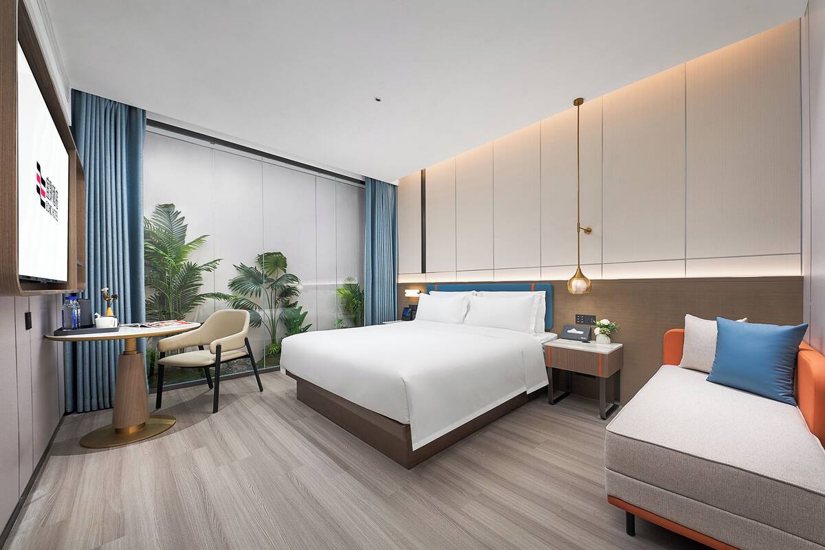 Una habitación de hotel moderna con una cama grande, un escritorio, una silla, una mesita de noche y un sofá.
