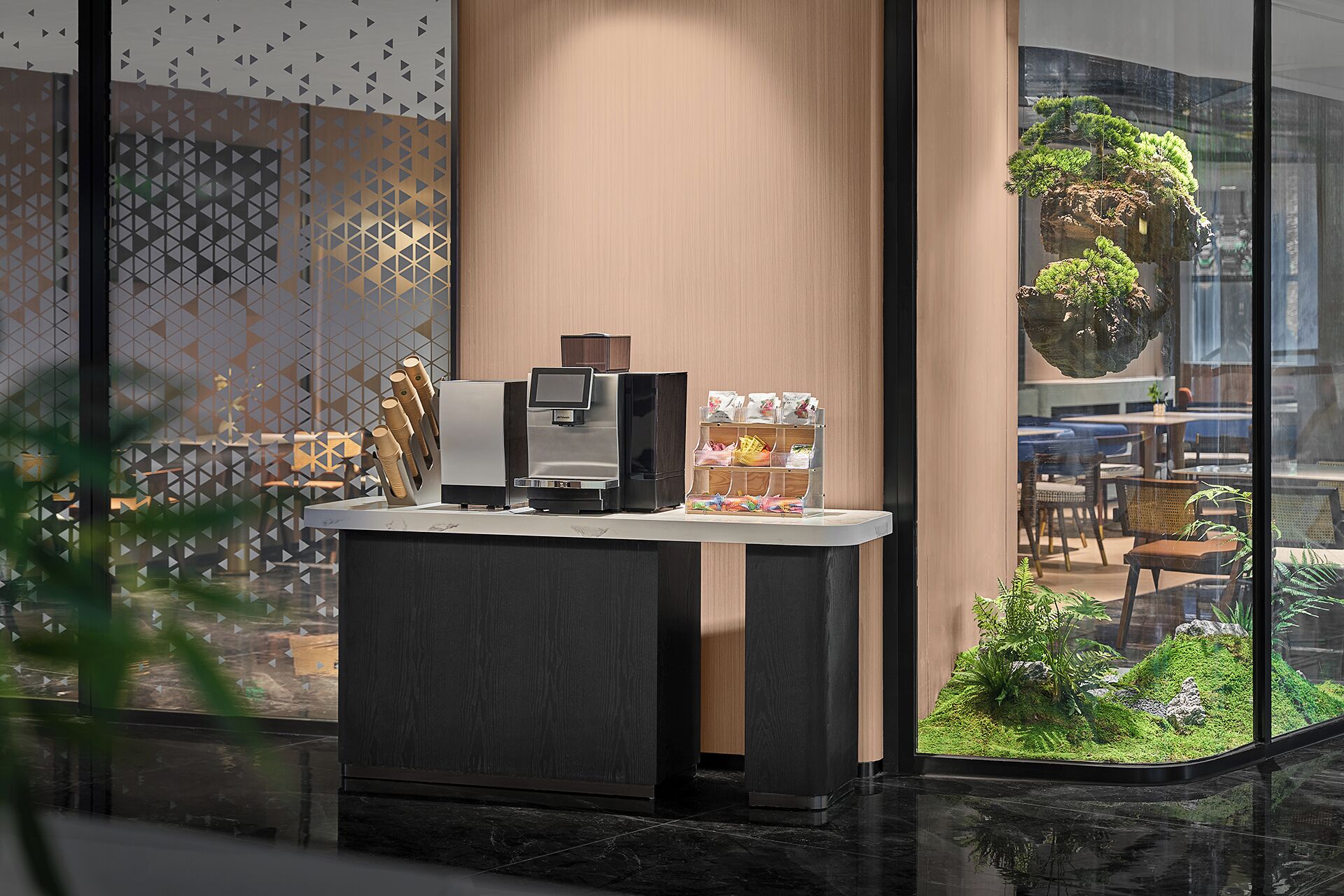 A modern reception desk with a coffee machine, a card reader, and a small plant display.