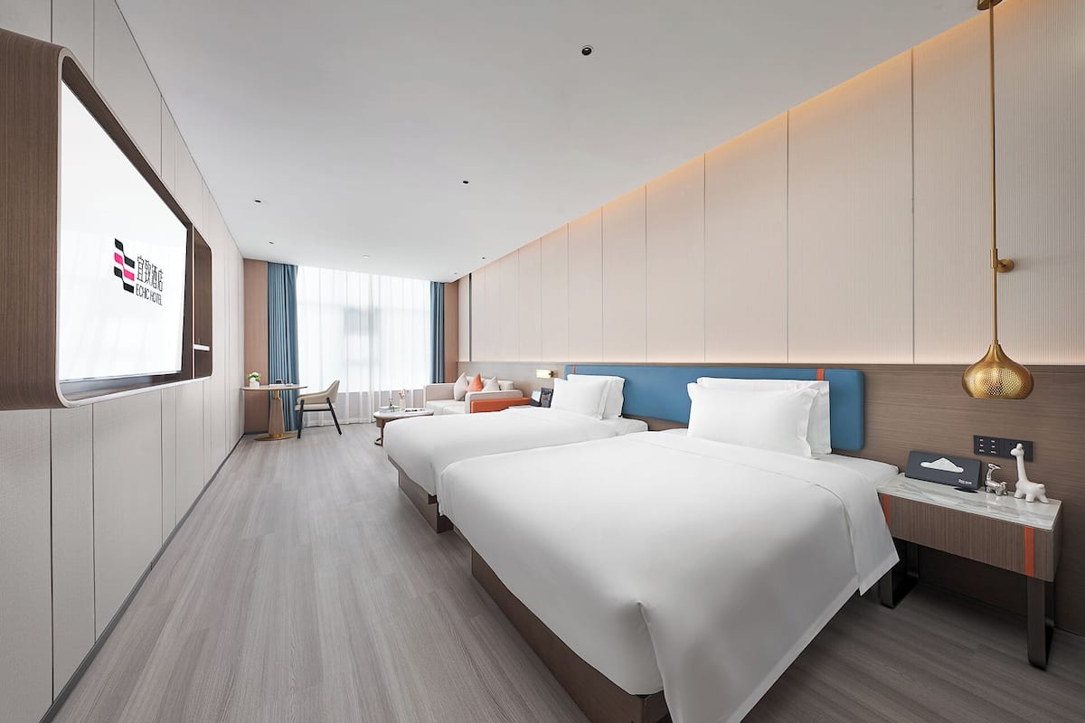 Habitación de hotel con dos camas, un escritorio, una silla y un ventanal grande.