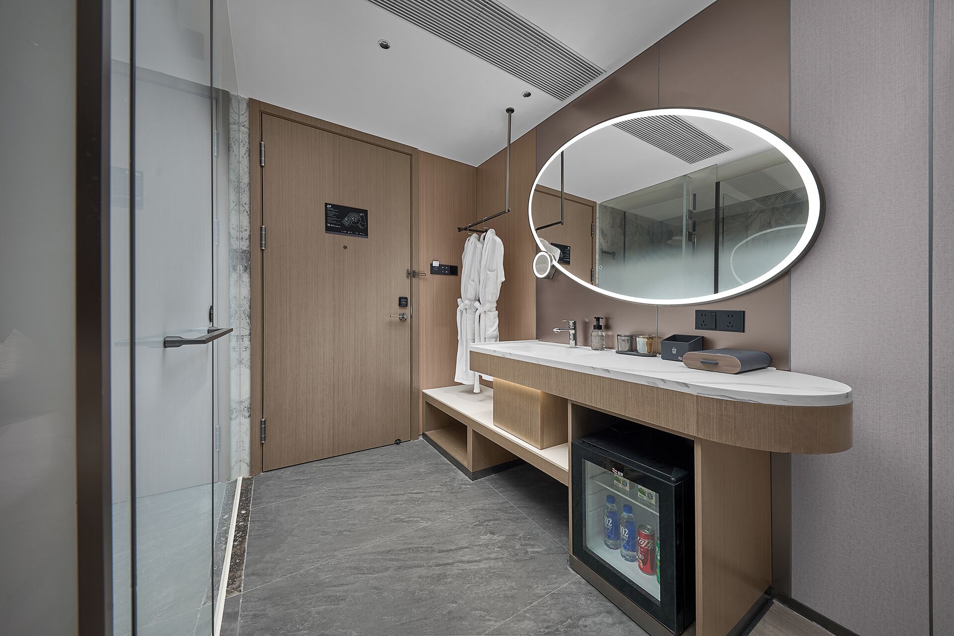A modern bathroom with a wooden vanity, a round mirror, and a glass shower enclosure.
