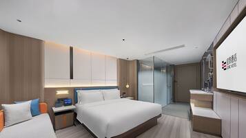 Una habitación de hotel moderna con una cama grande, un escritorio con computadora, cabina de ducha de vidrio y un minibar.