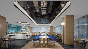 A modern dining area with a long table, blue cushioned chairs, and a central decorative piece.