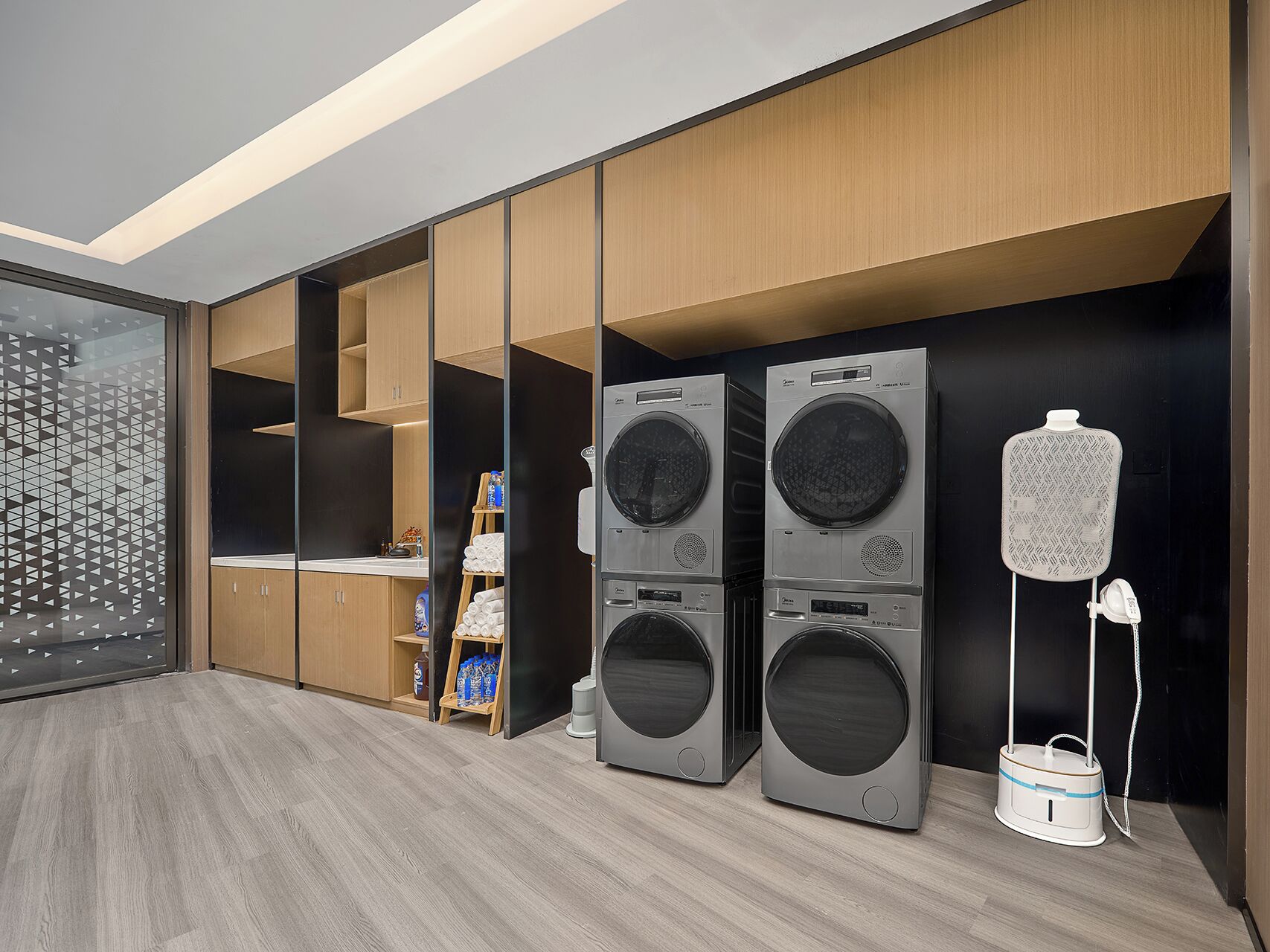 A modern laundry room with two stacked front-loading washing machines and a portable dryer.