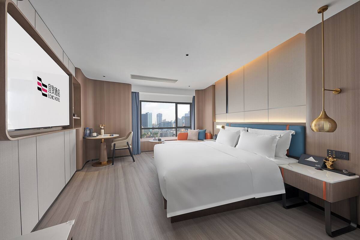 Una habitación de hotel moderna con una cama grande, un escritorio, una silla y vistas a la ciudad.