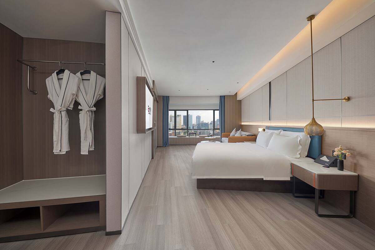 Una habitación de hotel moderna con una cama grande, mesitas de noche, un armario y vistas a la ciudad.