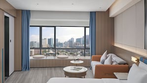 A modern hotel room with a large window, a sofa, a small table, and a bed.