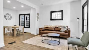 A spacious living area with a brown sofa, a round coffee table, and a dining table with chairs.