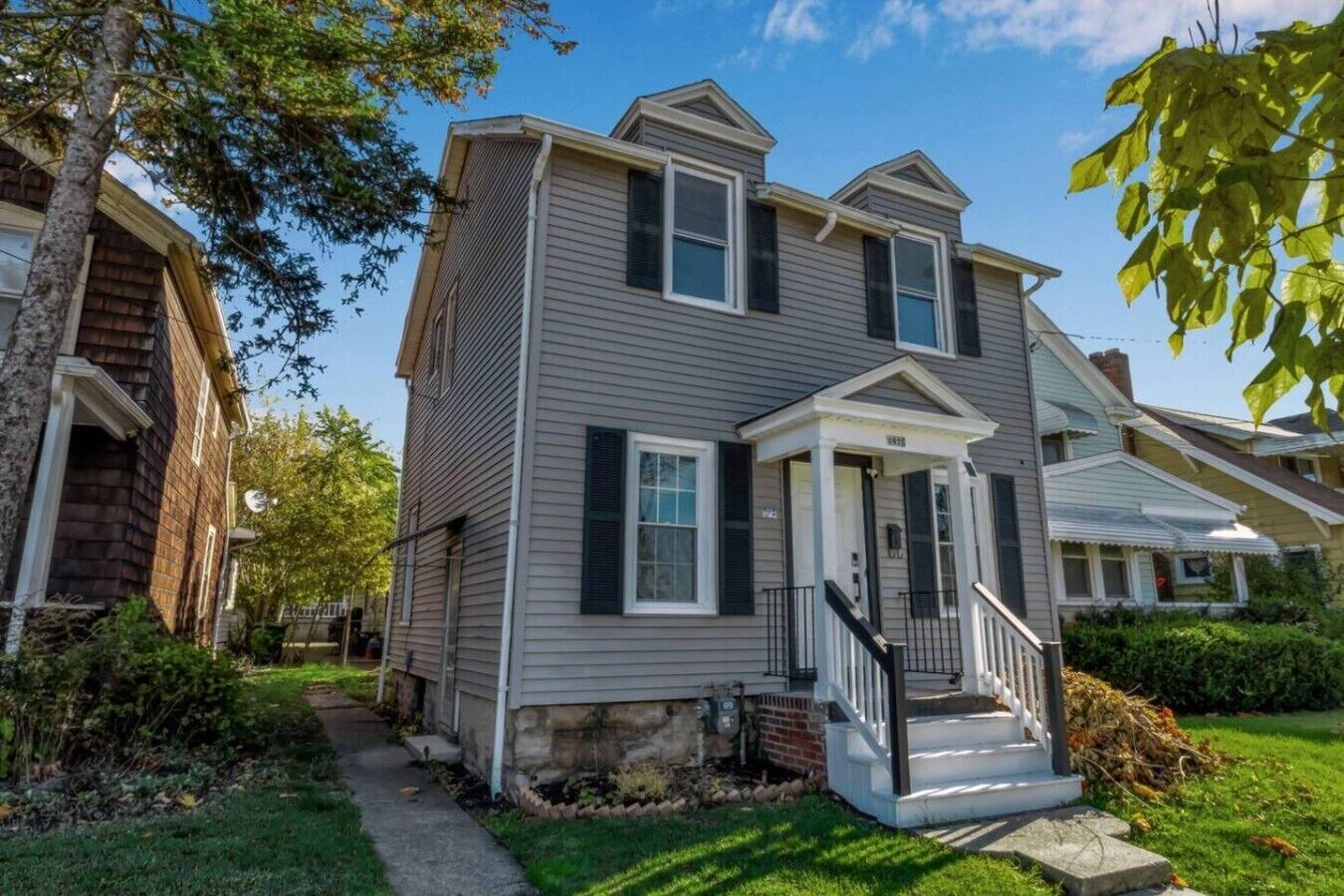 A two-story house with a front porch, a small front yard, and a neighboring house.