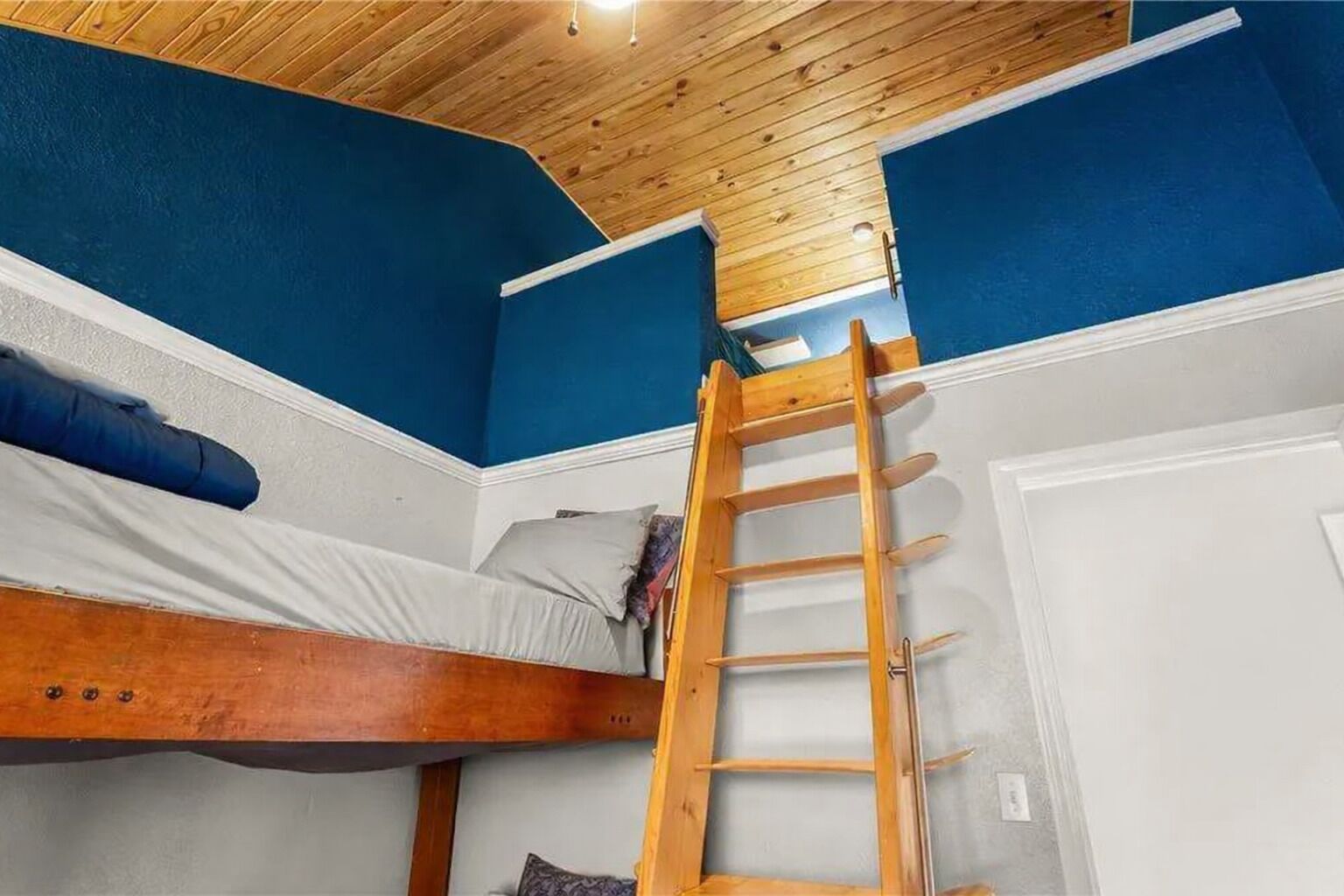 Habitación con literas, una escalera de madera, paredes azules y techo de madera.