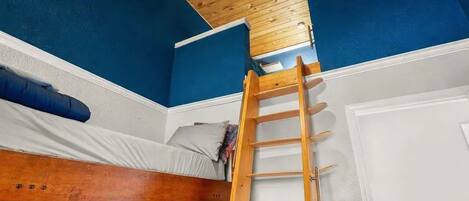 Habitación con literas, una escalera de madera, paredes azules y techo de madera.