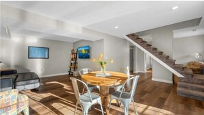 Amplia sala de estar con una mesa de comedor de madera, sillas metálicas, una escalera y un sofá.