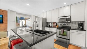 Una cocina moderna con armarios blancos, electrodomésticos de acero inoxidable, una isla grande con fregadero y vistas al exterior.