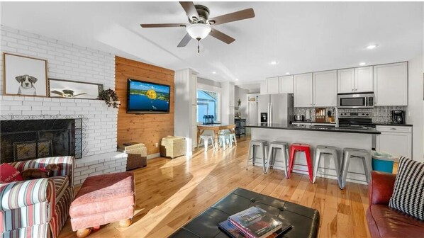 A modern living room with a fireplace, a TV mounted on the wall, and a kitchen area with white cabinets and a microwave.