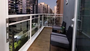 Ein Balkon mit Blick auf umliegende Gebäude, einer Glastür und einer Sitzgelegenheit mit Tisch und Stühlen.