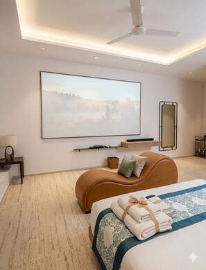 A modern bedroom with a large bed, a sofa bed, a ceiling fan, a mounted TV, a bedside table, and a mirror. - Hotel VD Rooms Althan (Surat)