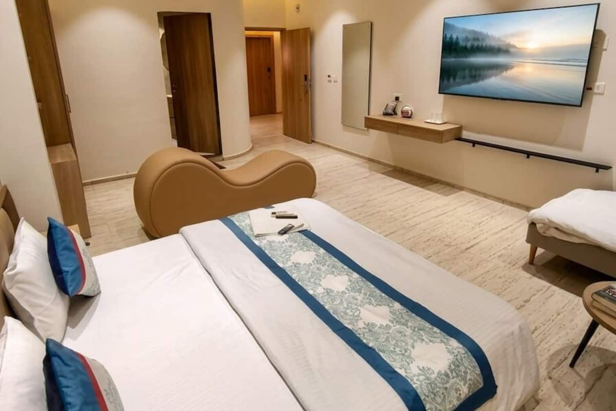 A modern hotel room with a large bed, a flat-screen TV, a seating area, and a view of a forested landscape.