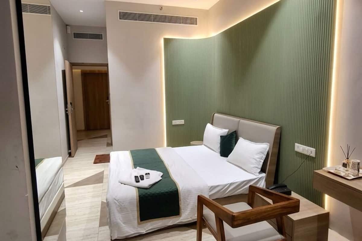 A modern hotel room with a bed, bedside table, chair, and a mirror.