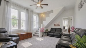 A living room with a ceiling fan, a staircase, leather sofas, and a large window. - Hidden Nature Haven - Stylish Comfort near Cincy (Park Hills)