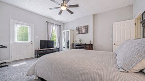 A bedroom with a bed, ceiling fan, TV, and a door leading to another room. - Hidden Nature Haven - Stylish Comfort near Cincy (Park Hills)