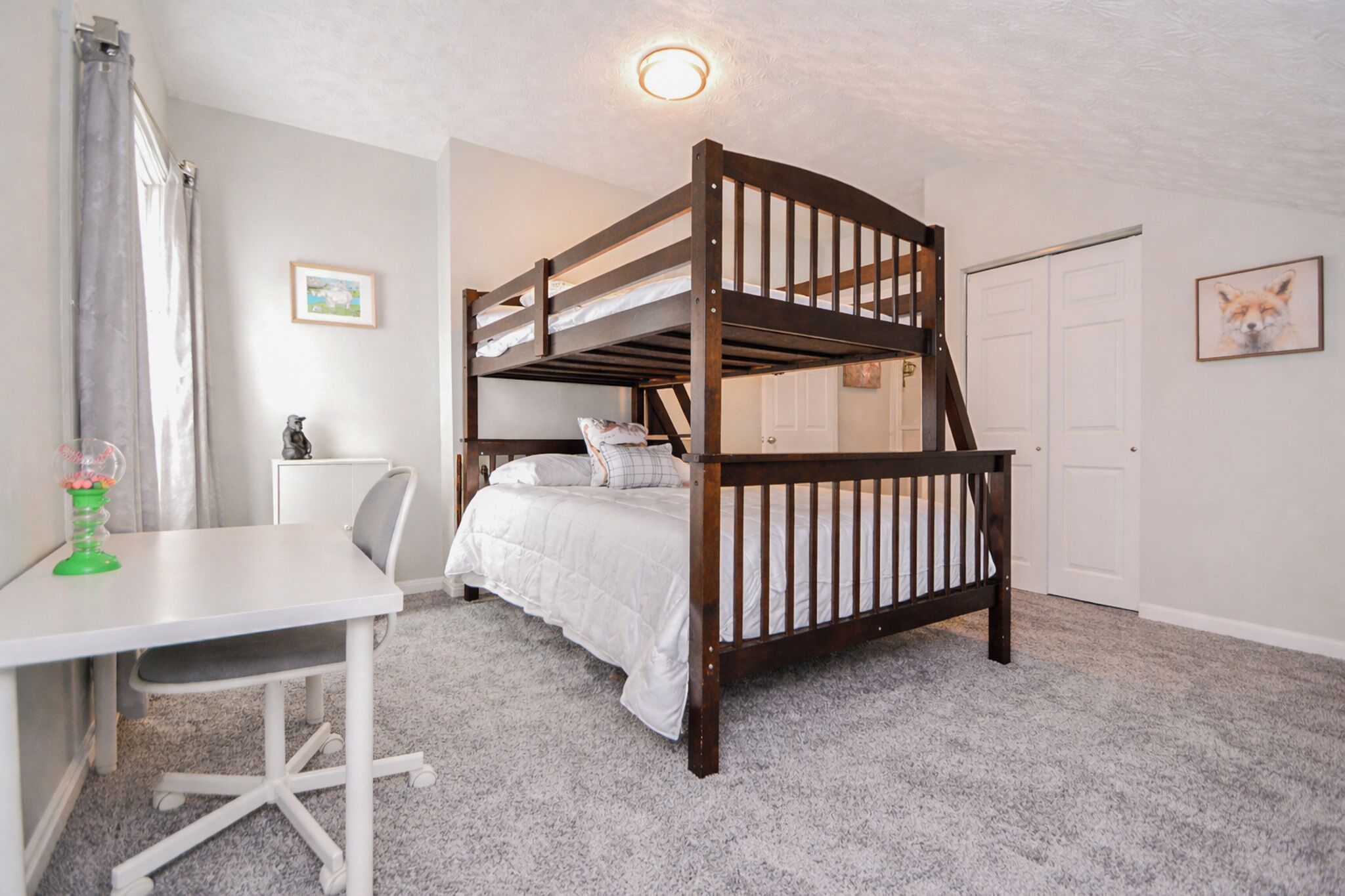 A bunk bed in a room with a desk and chair, a door, and a framed picture on the wall.