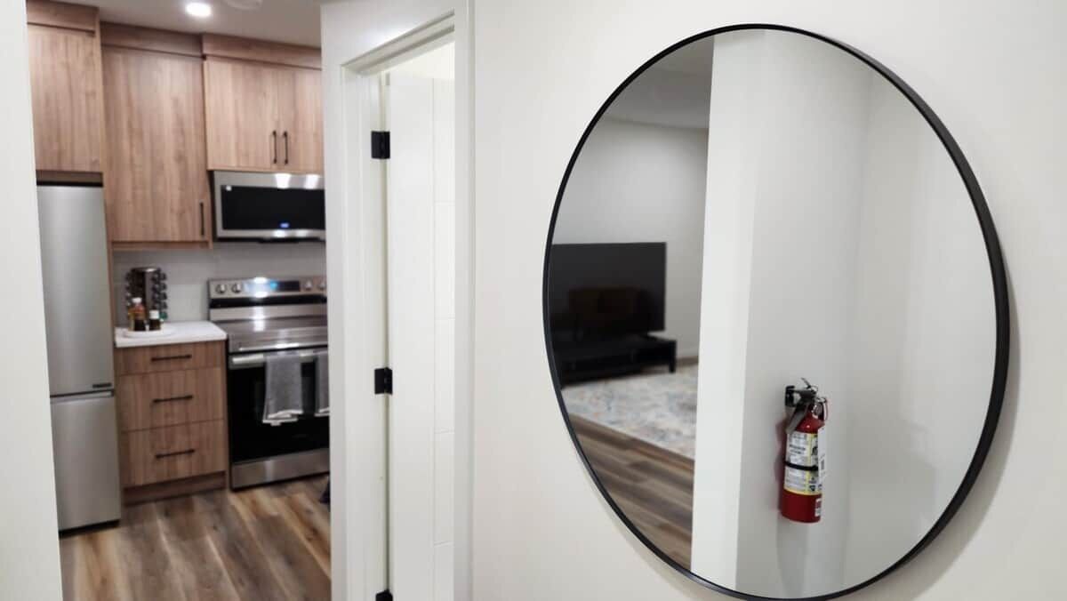 A modern kitchen with wooden cabinets, stainless steel appliances, and a round mirror on the wall.
