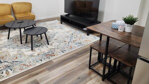 Un soggiorno con televisore, due poltrone gialle, un tavolino, un tappeto e un piccolo tavolo con oggetti decorativi.