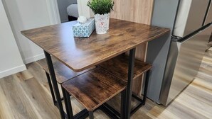 Una cucina con un tavolo di legno, due panche, un frigorifero e una pianta in vaso.