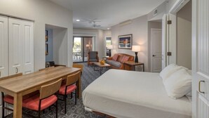 Ein Hotelzimmer mit Bett, Esstisch mit Stühlen, Sofa, Sessel, Lampe und Deckenventilator.