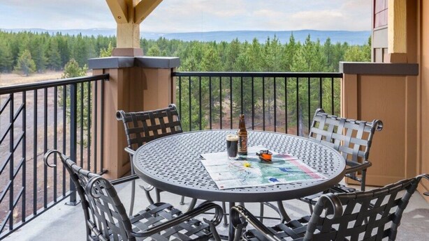 Ein runder Metalltisch mit vier Stühlen auf einem Balkon mit Blick auf einen Wald und Berge.