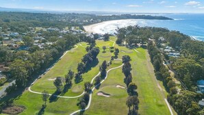 Luchtbeeld van een golfbaan met een kustlandschap op de achtergrond, omgeven door woonwijken.
