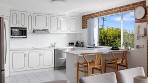 Een moderne keuken met witte kasten, roestvrijstalen apparatuur, een groot raam en een eethoek met houten stoelen.